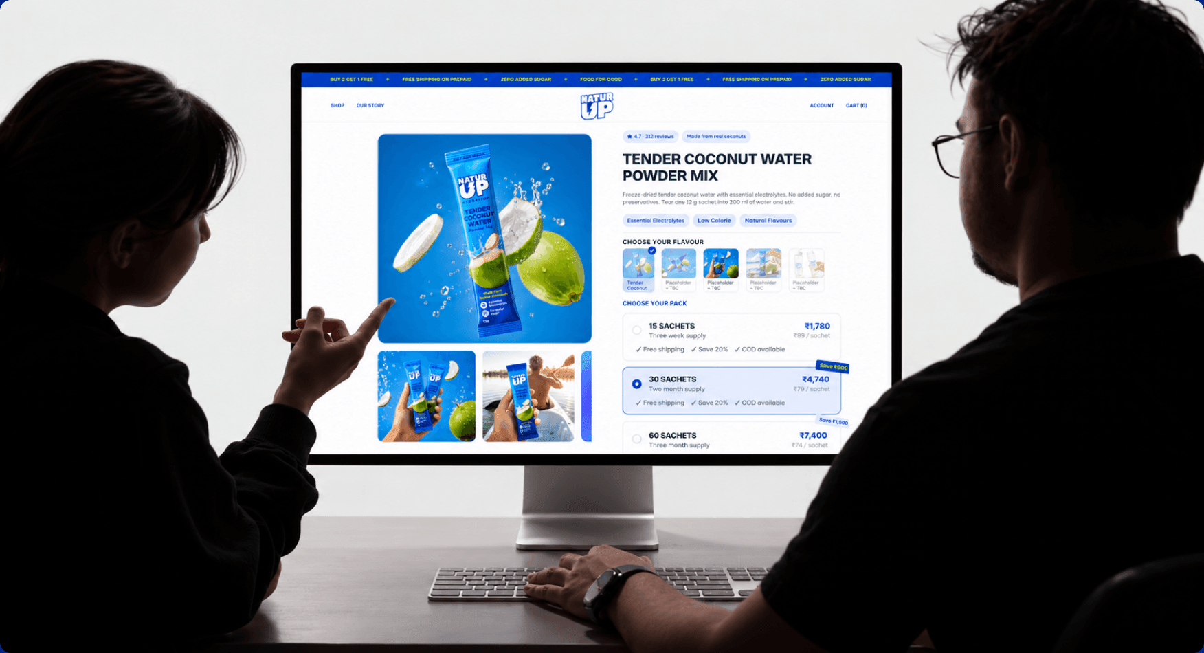 Two people reviewing the new NaturUp product page on a large monitor