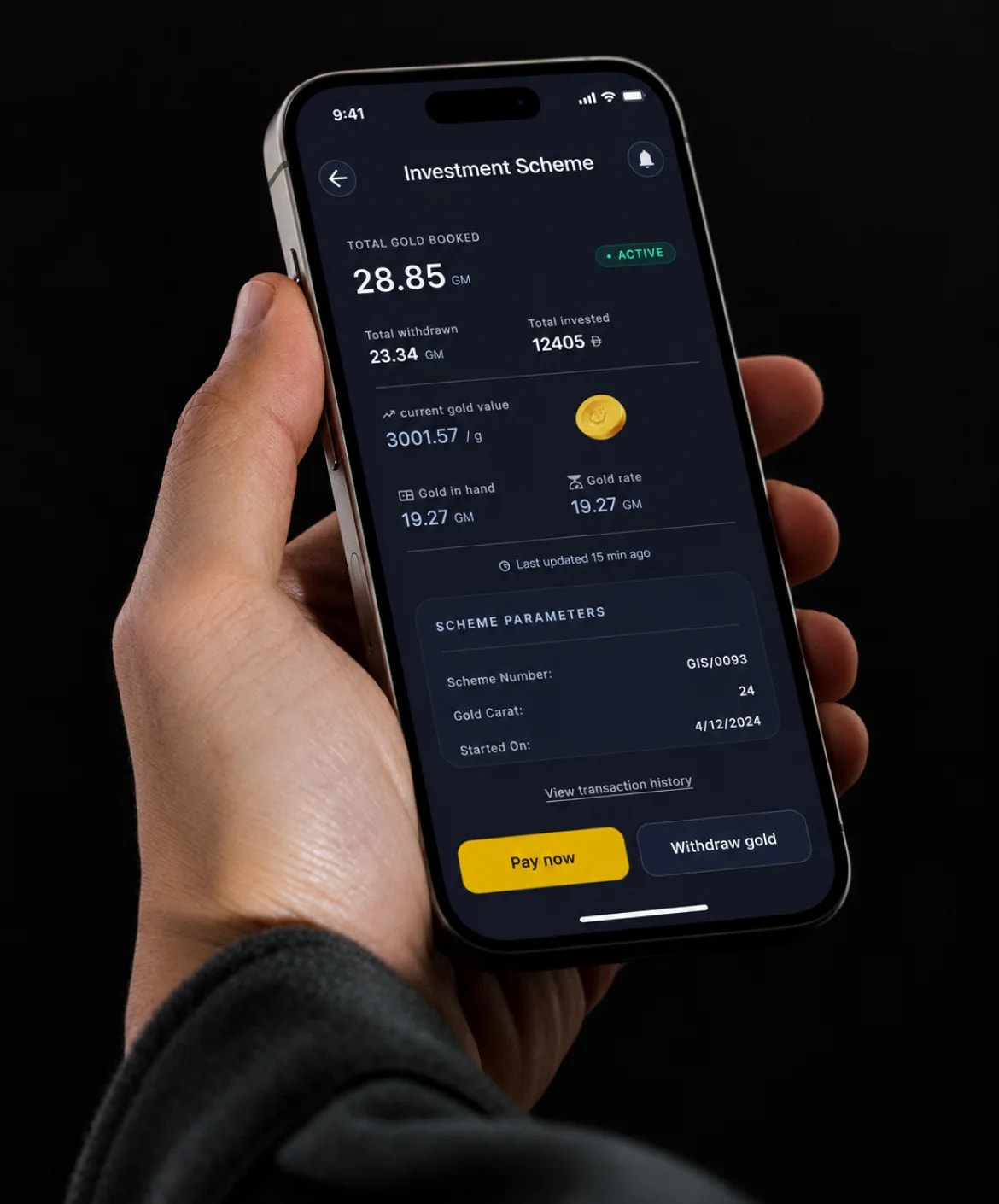 A hand holding a phone open on the Investment Scheme screen, with total gold booked, gold in hand and Pay now and Withdraw gold buttons