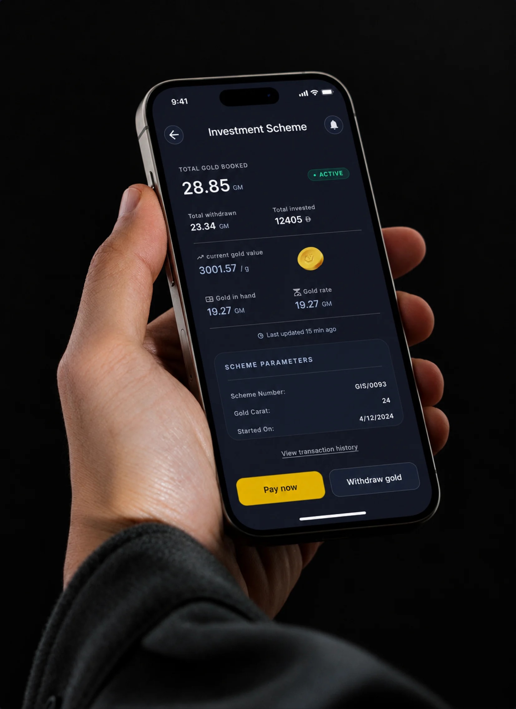 A hand holding a phone open on the Investment Scheme screen, with total gold booked, gold in hand and Pay now and Withdraw gold buttons