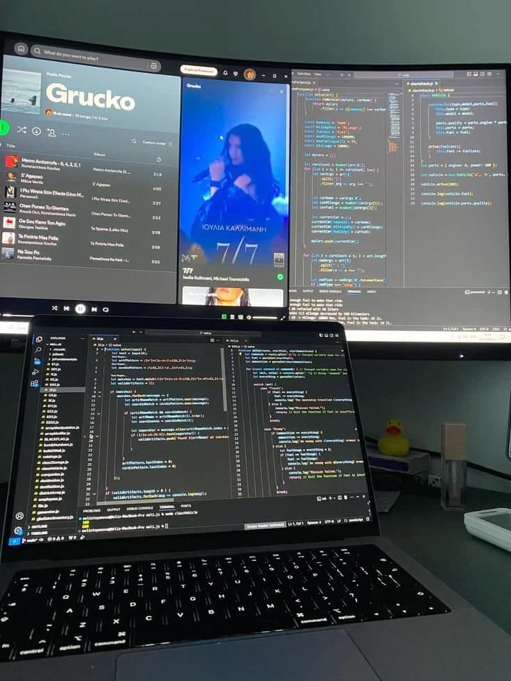 Code open on a laptop and across the monitors behind it